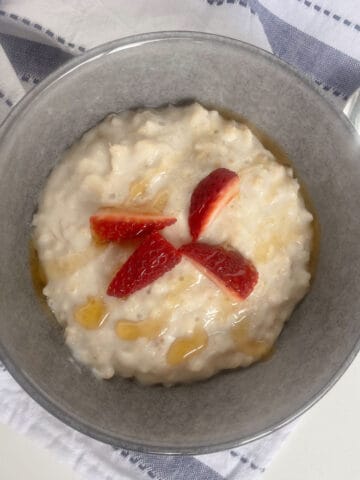 Porridge topped with honey and strawberries in a grey bowl.
