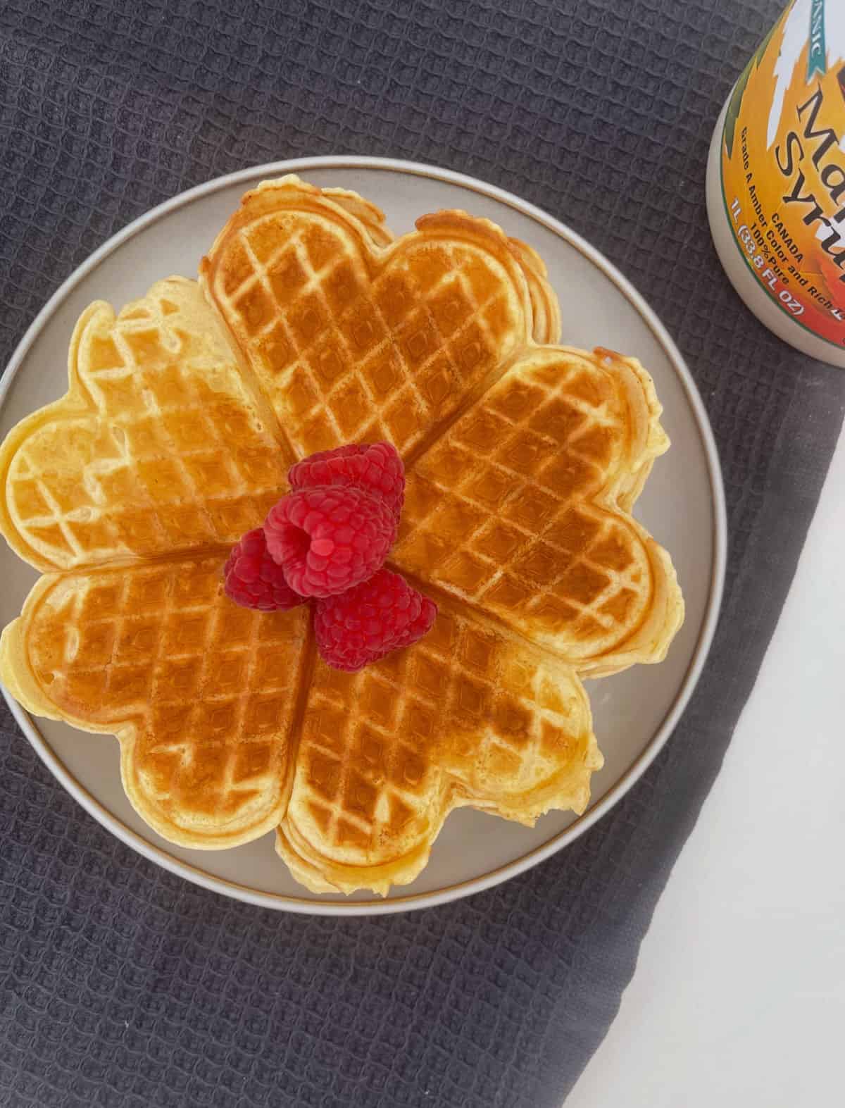 Overhead view of waffles on a grey plate topped with raspberries