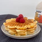 Side view of waffles on a grey plate topped with raspberries.