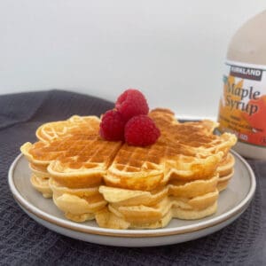 Side view of waffles on a grey plate topped with raspberries.
