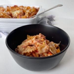 Black bowl with BBQ Chicken Pasta Bake with white dish in the background.