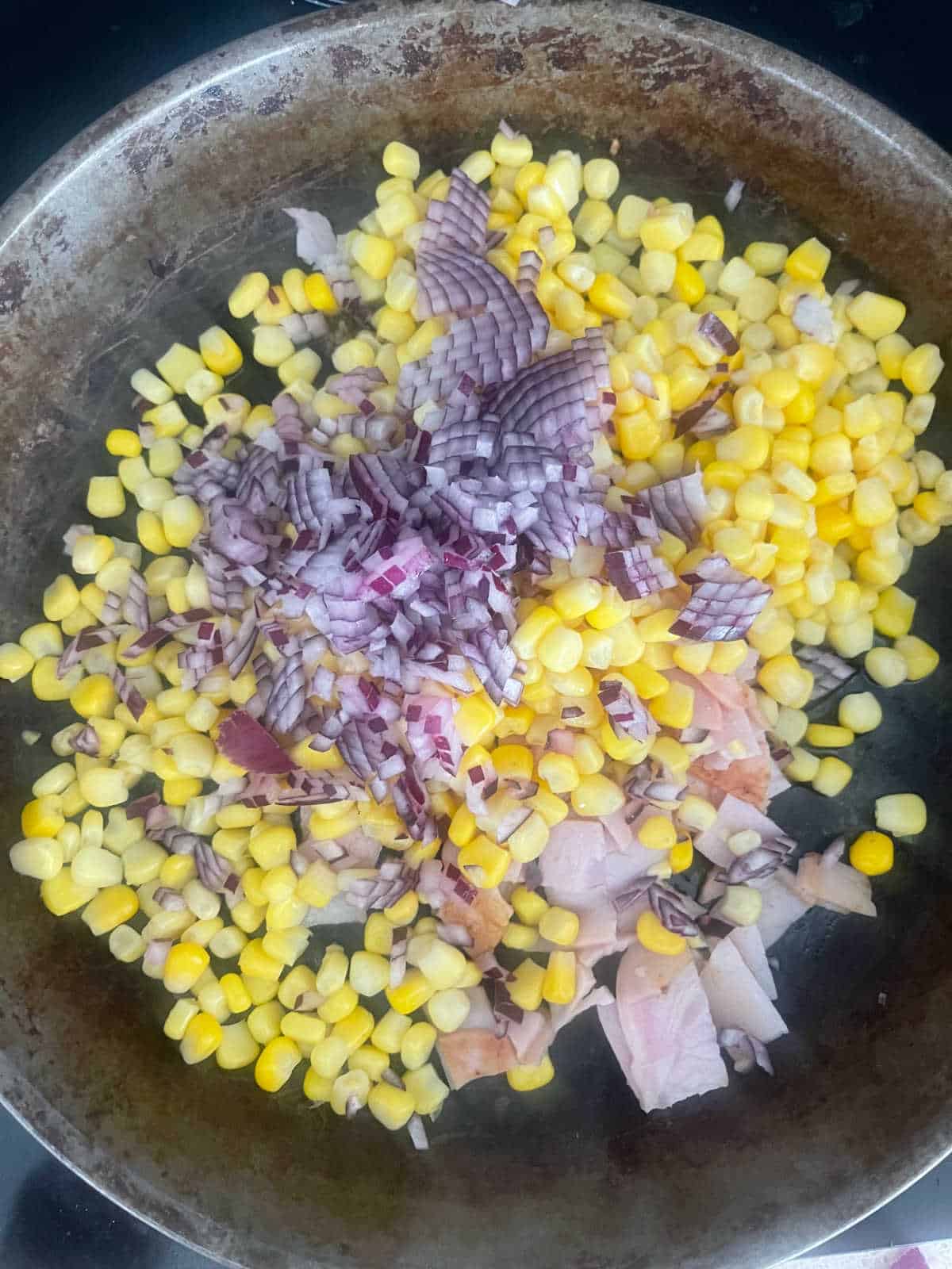 corn, bacon and red onion in a frying pan.