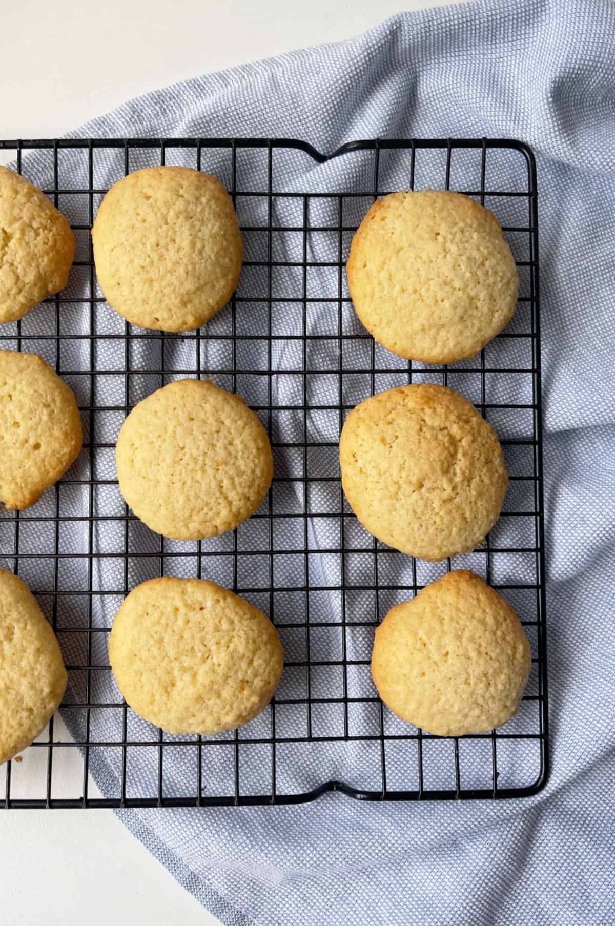 Coconut Biscuits on a black wire cooling rack that is sitting on a blue towel.