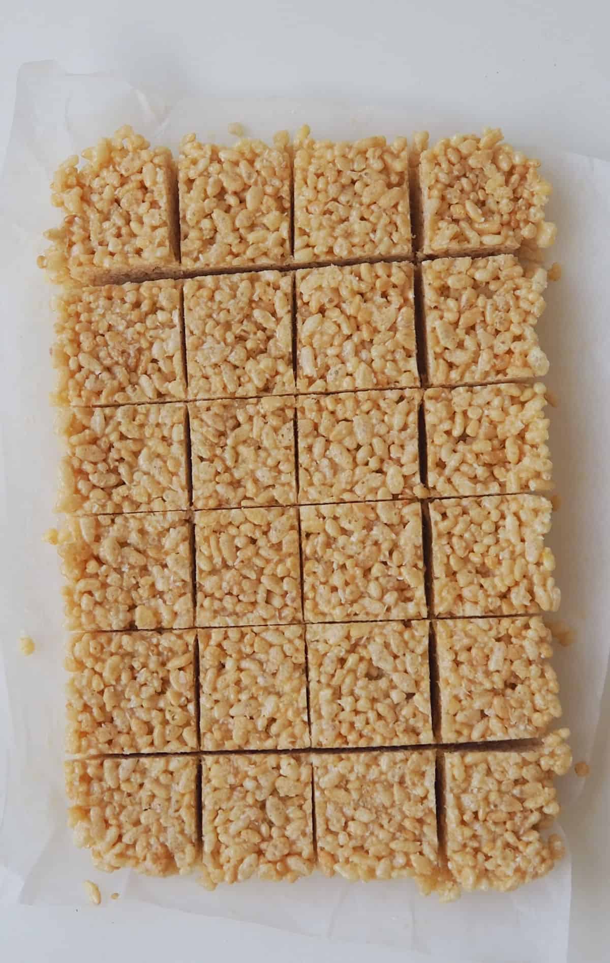 Overhead view of rice bubble slice sitting on a sheet of baking paper and cut into pieces.