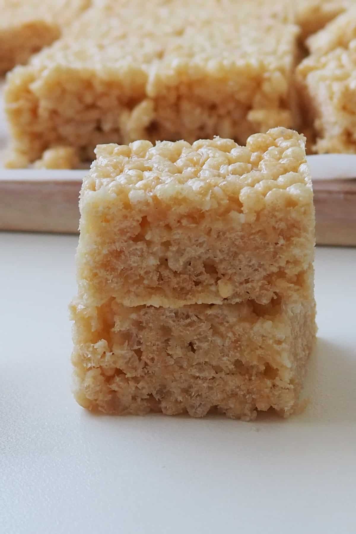 Two pieces of Rice Bubble Slice on top of each other. In the background is a timber tray with more pieces.