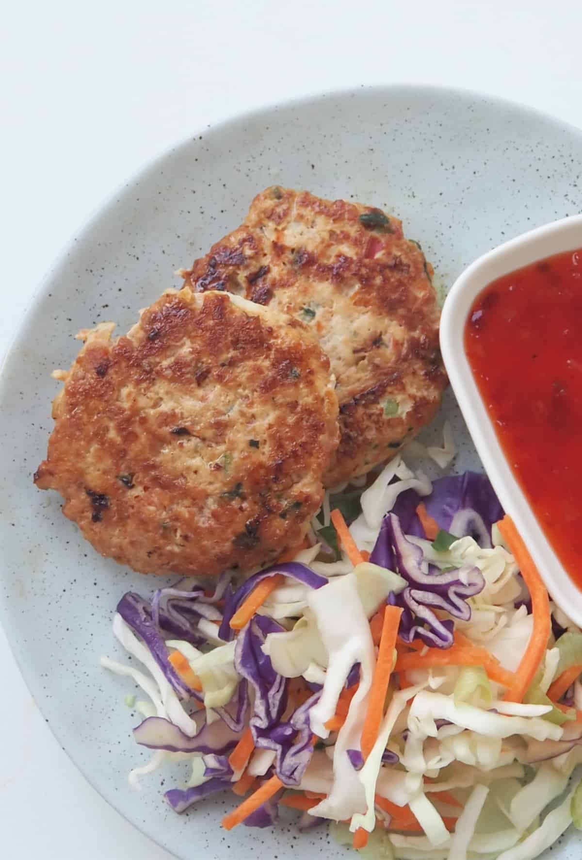 Overhead view of chicken rissoles on a green plate served with coleslaw and sweet chilli sauce.