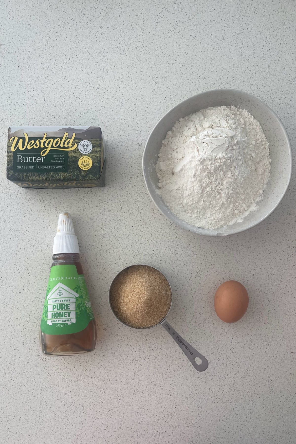 Ingredients to make Honey Biscuits on a speckled bench.