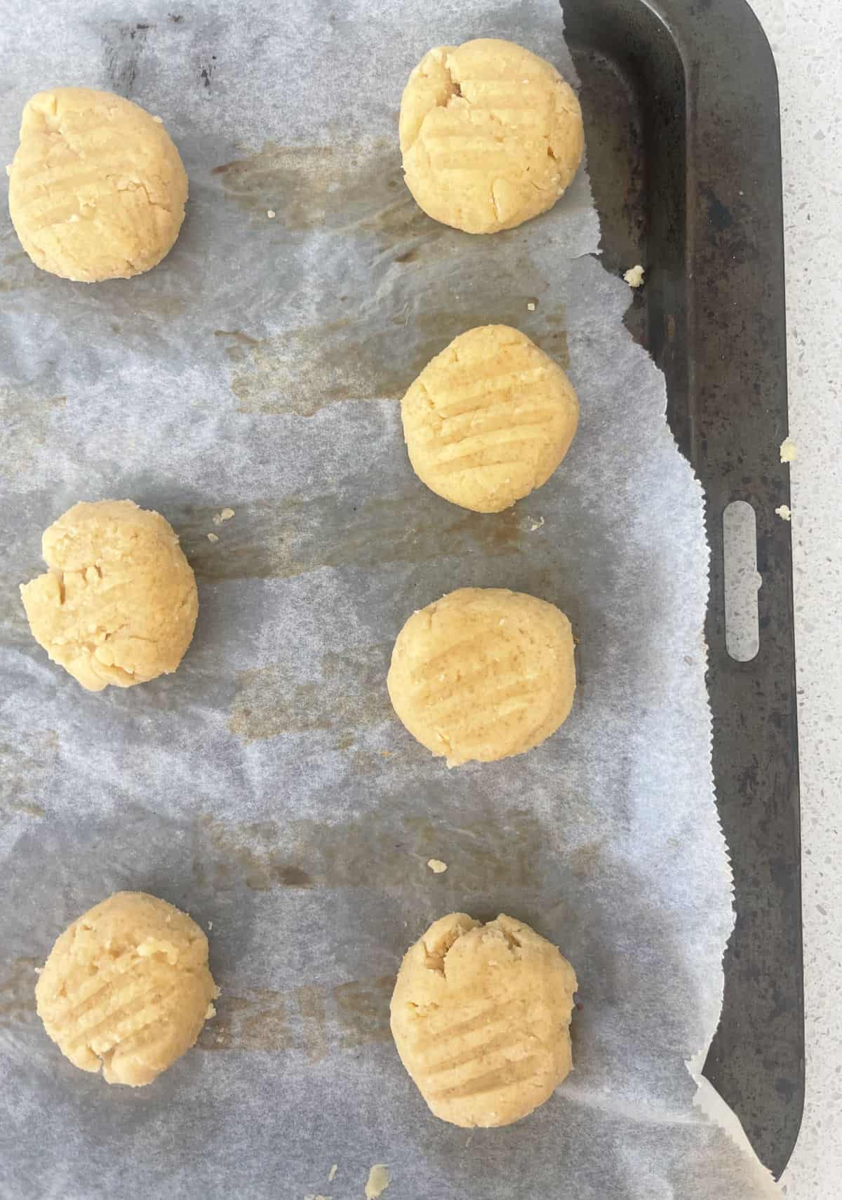 Honey Biscuits pushed down with a fork and sitting on a baking tray.