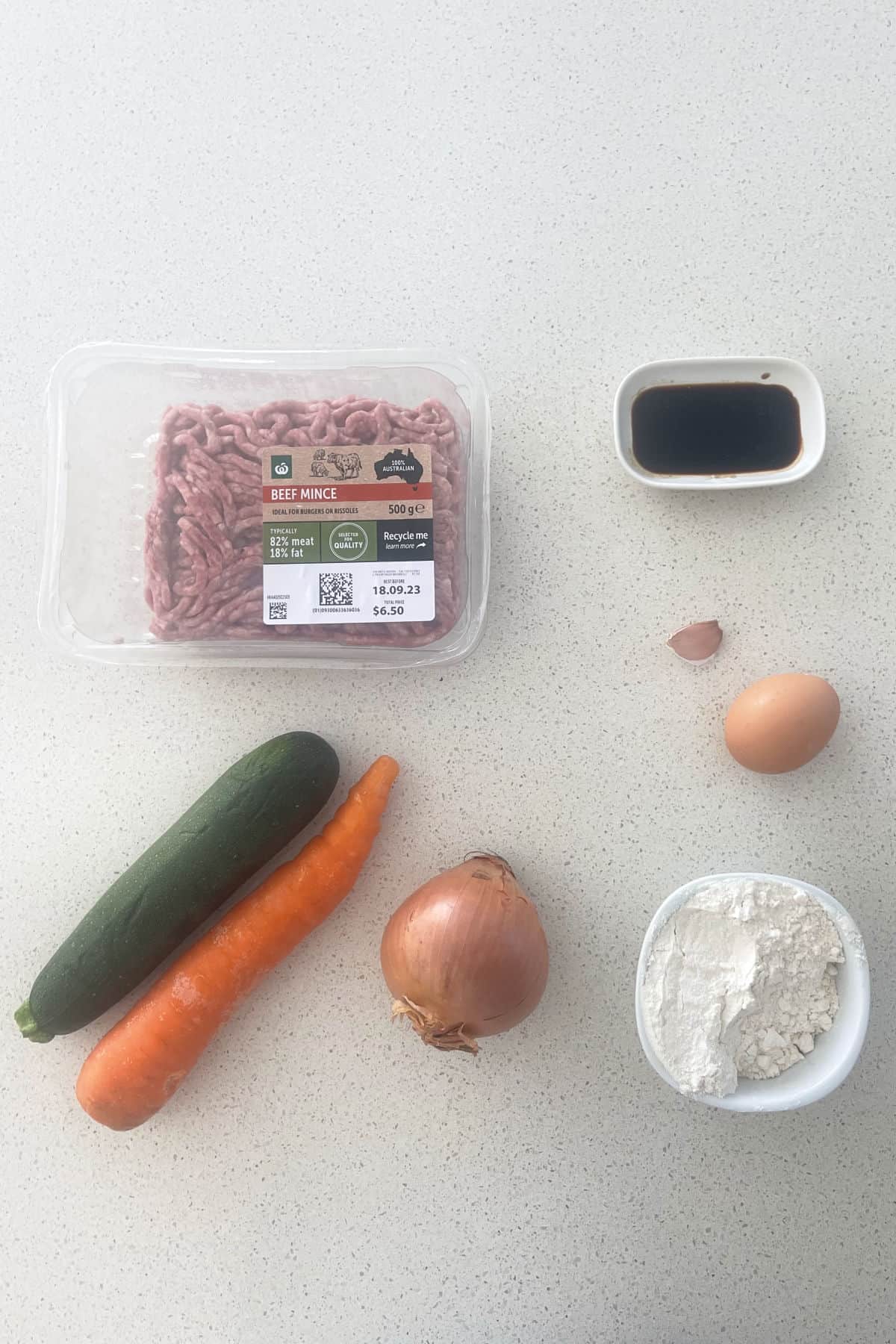 Ingredients to make Beef Rissoles sitting on a speckled bench top.