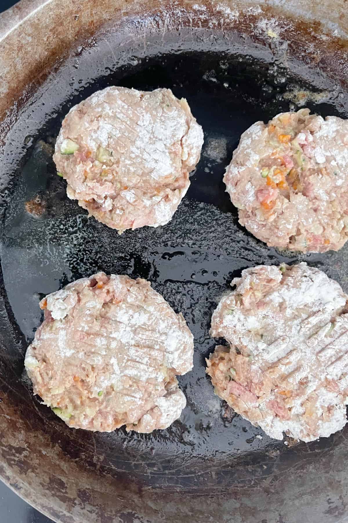 Beef Rissoles cooking in a cast iron frying pan.