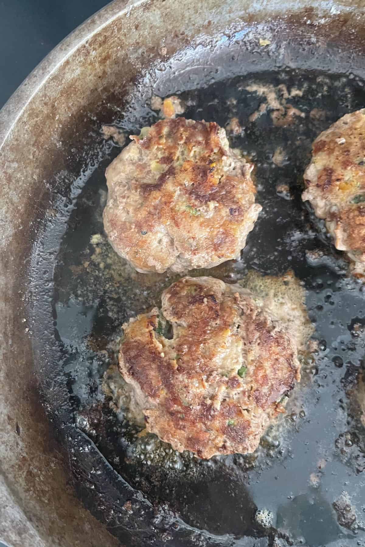 Beef rissoles cooking in a cast iron frying pan.