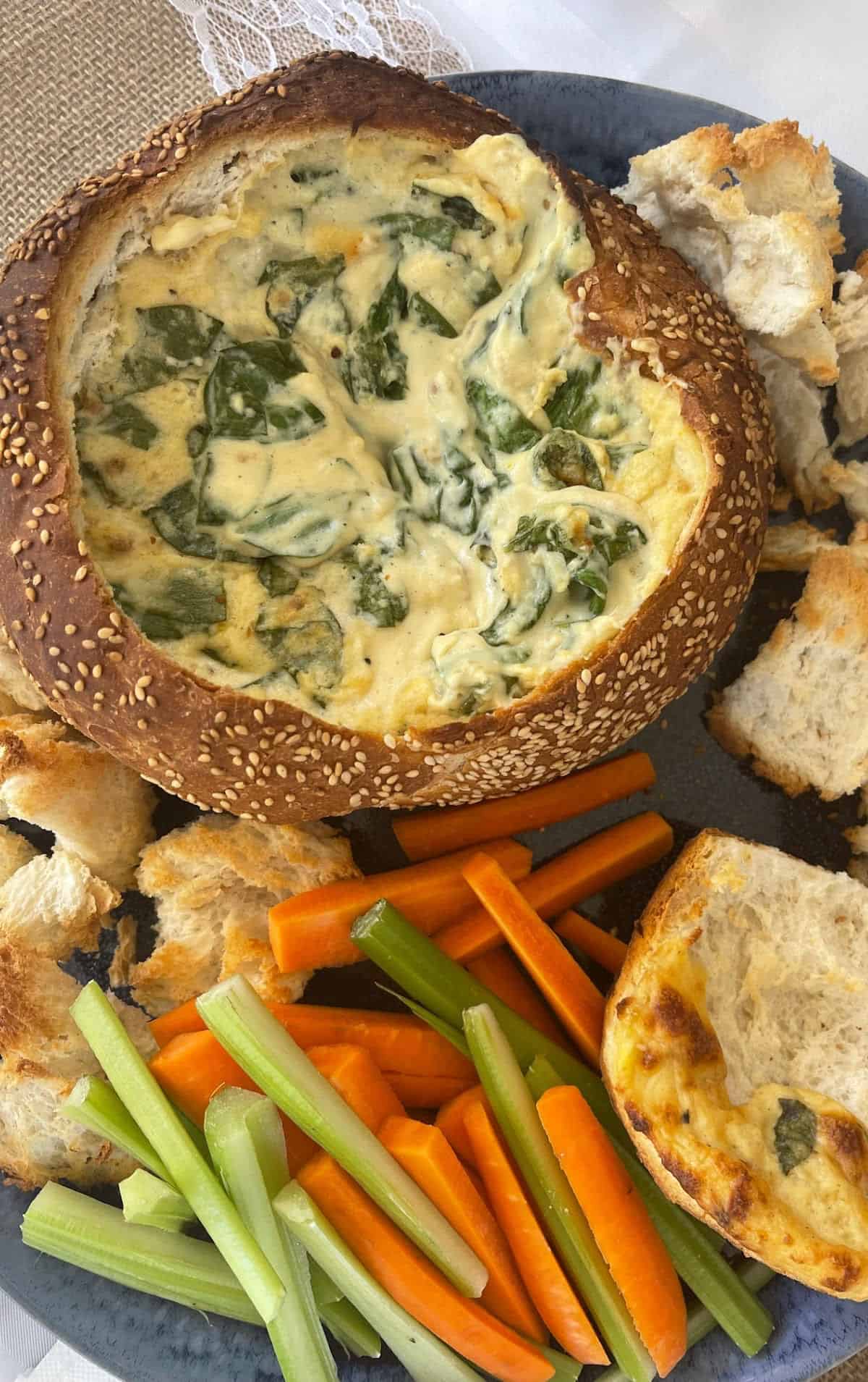 Overhead view of spinach cob loaf on a blue serving tray surrounded by veggie sticks and bread pieces.