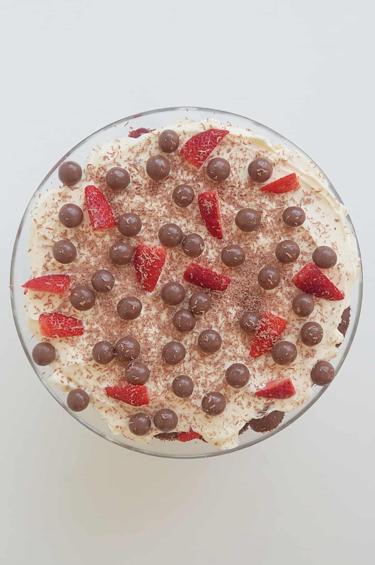 Overhead view of chocolate trifle in a glass bowl topped with strawberries, Maltesers and chocolate.