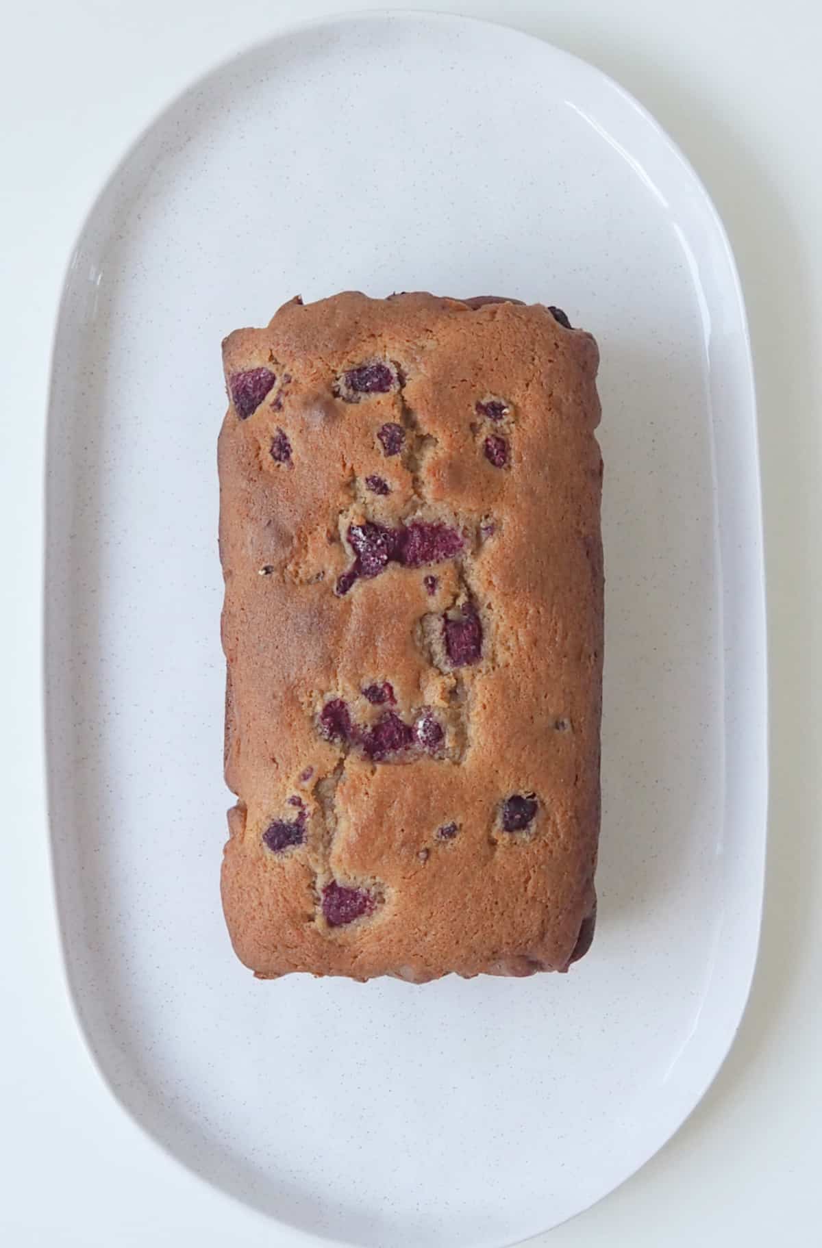 Overhead view of Banana and Raspberry Loaf unsliced on a platter.