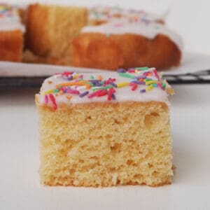 Slice of Vanilla Sheet Cake sitting in front of a wire rack.