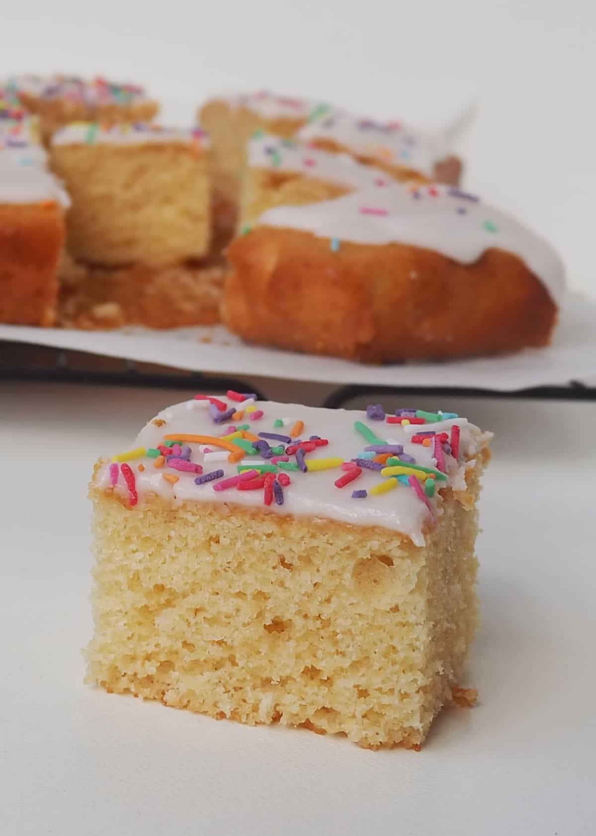 Side view of a Slice of Vanilla Sheet Cake sitting in front of a wire rack.