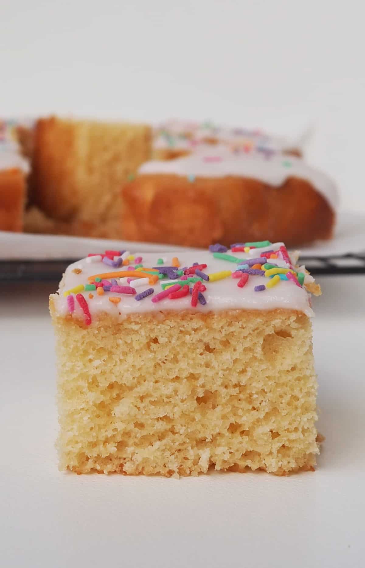 Slice of Vanilla Sheet Cake sitting in front of a wire rack.