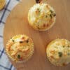 Three savoury cheese and corn muffins on a round wooden board.