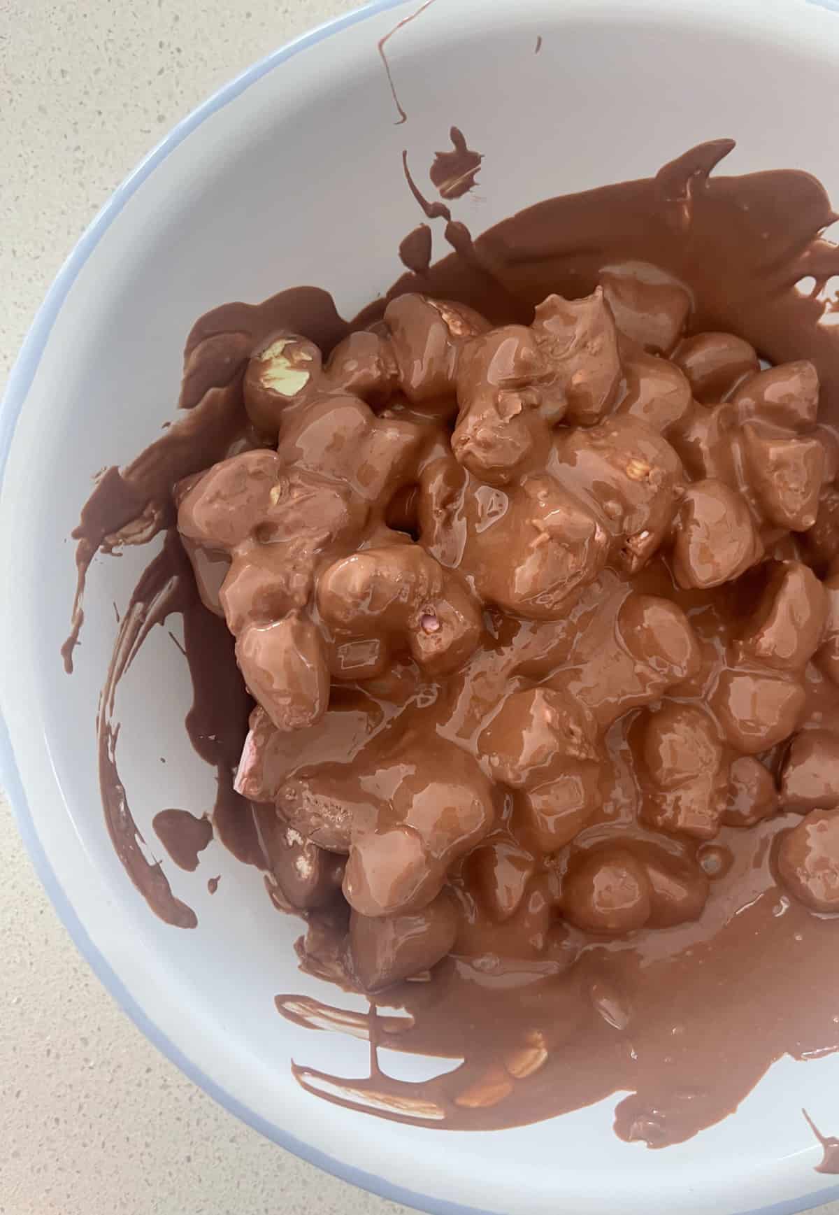 Melted chocolate over rock road ingredients in a white bowl.