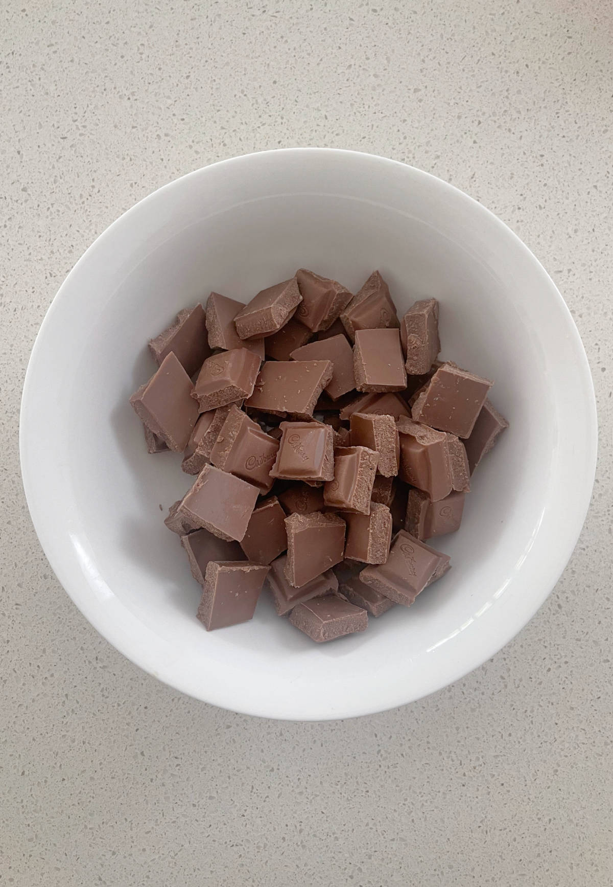 Milk chocolate squares in a white bowl.