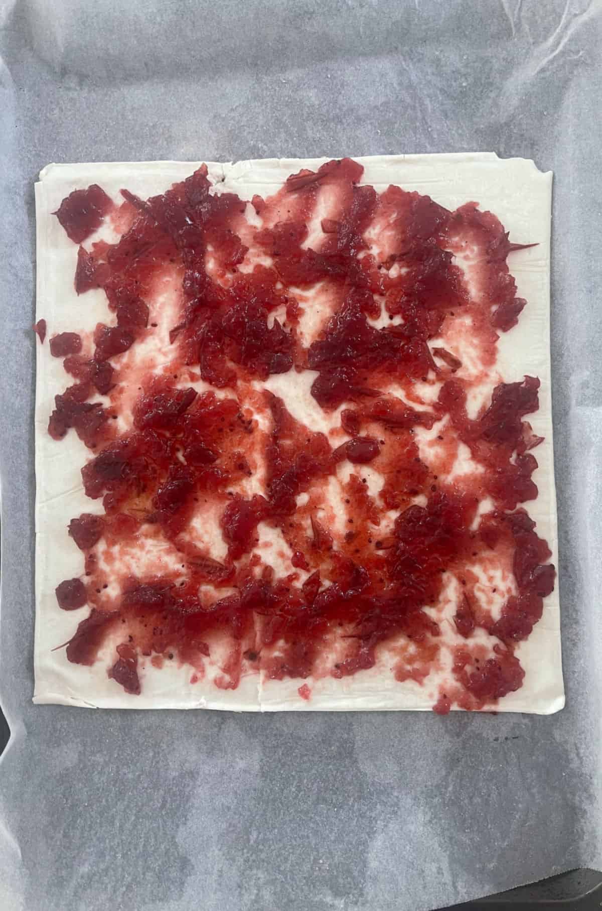 A sheet of puff pastry covered with cranberry sauce