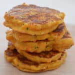 Stack of five sweet potato fritters sitting on a pale wooden plate.