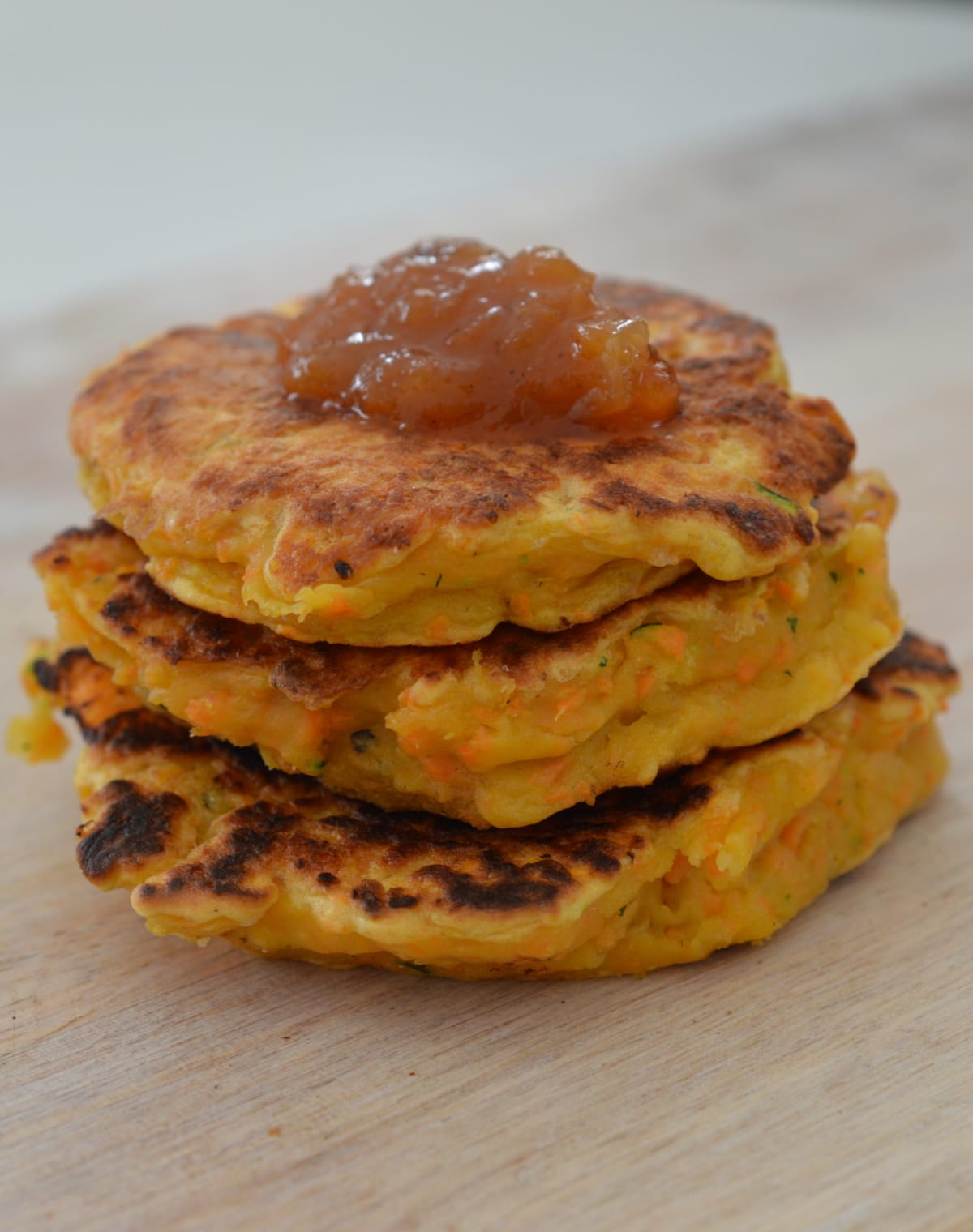 Three sweet potato fritters on a wooden plate, they are topped with homemade tomato relish.