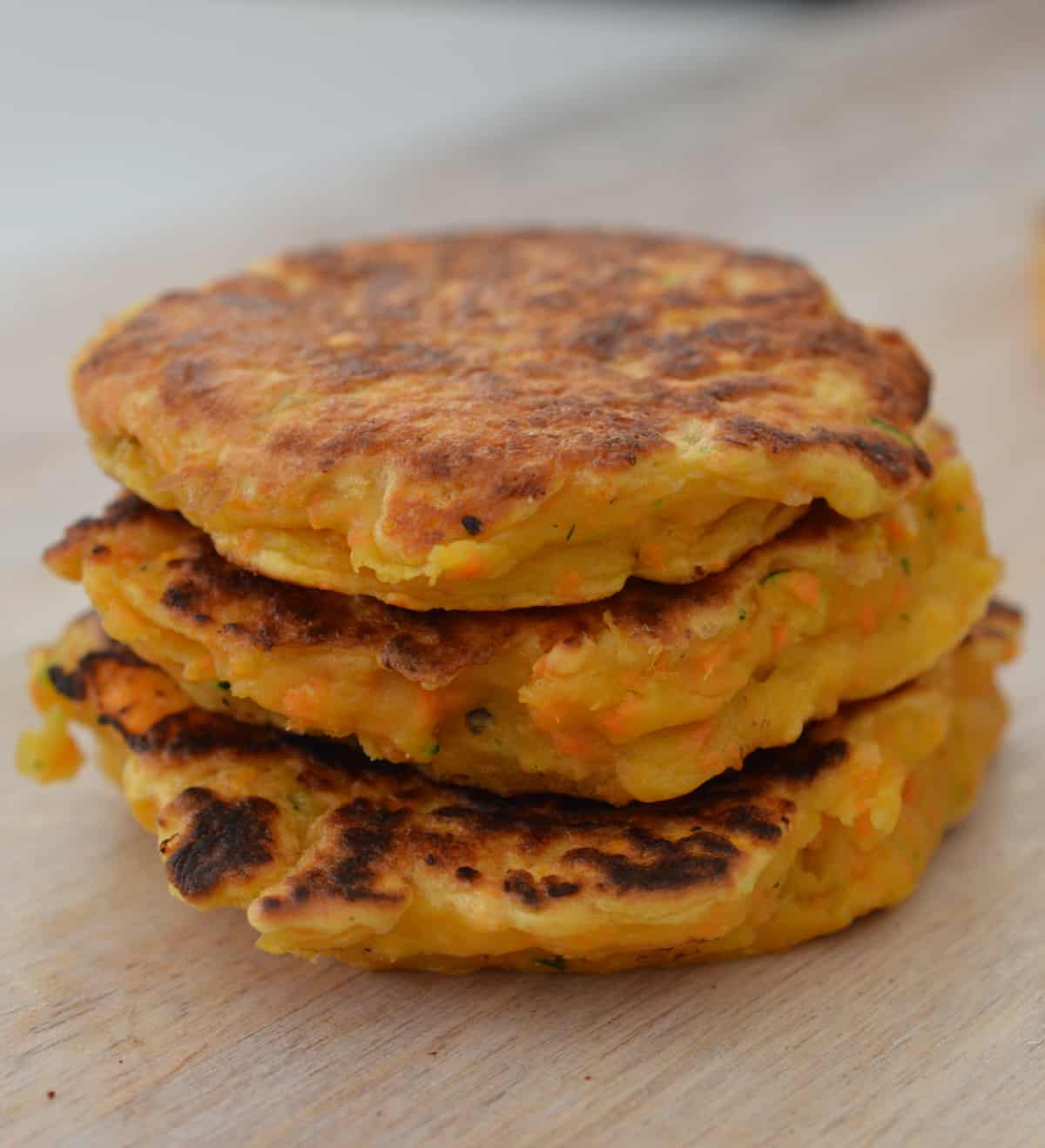 Stack of three sweet potato fritters sitting on a wooden plate.