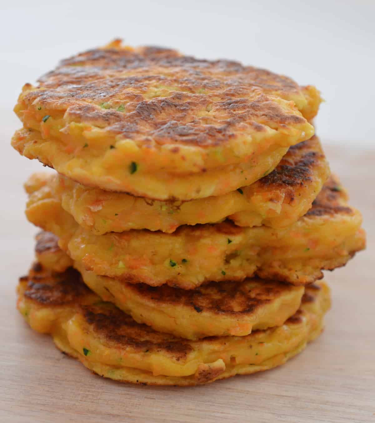 Stack of five sweet potato fritters sitting on a pale wooden plate.