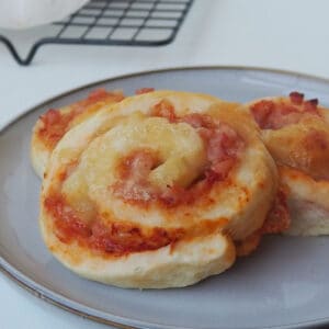 Three Pizza Scrolls sitting on a grey plate. In the background is a black wire cooling rack.