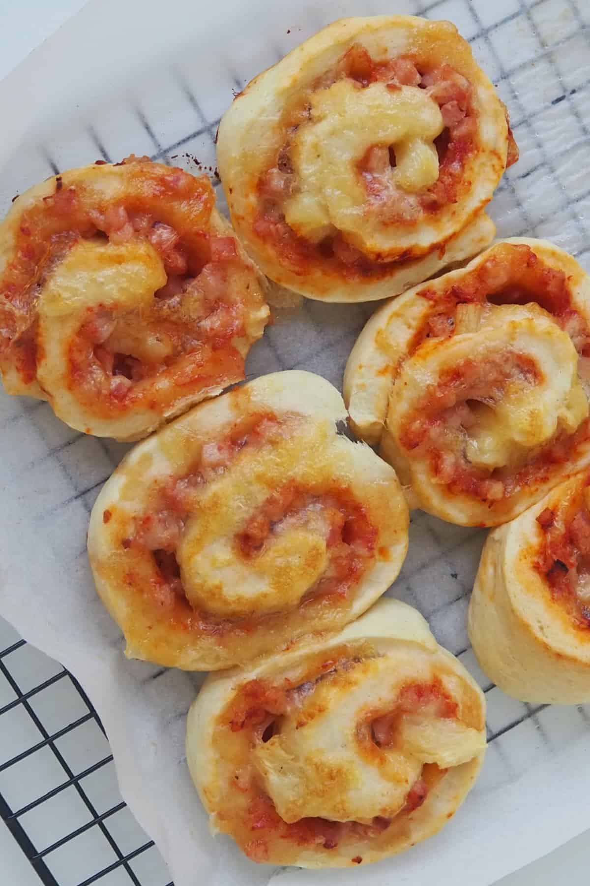 Overhead view of Pizza Scrolls sitting on a sheet of baking paper that is on top of a black wire cooling rack.