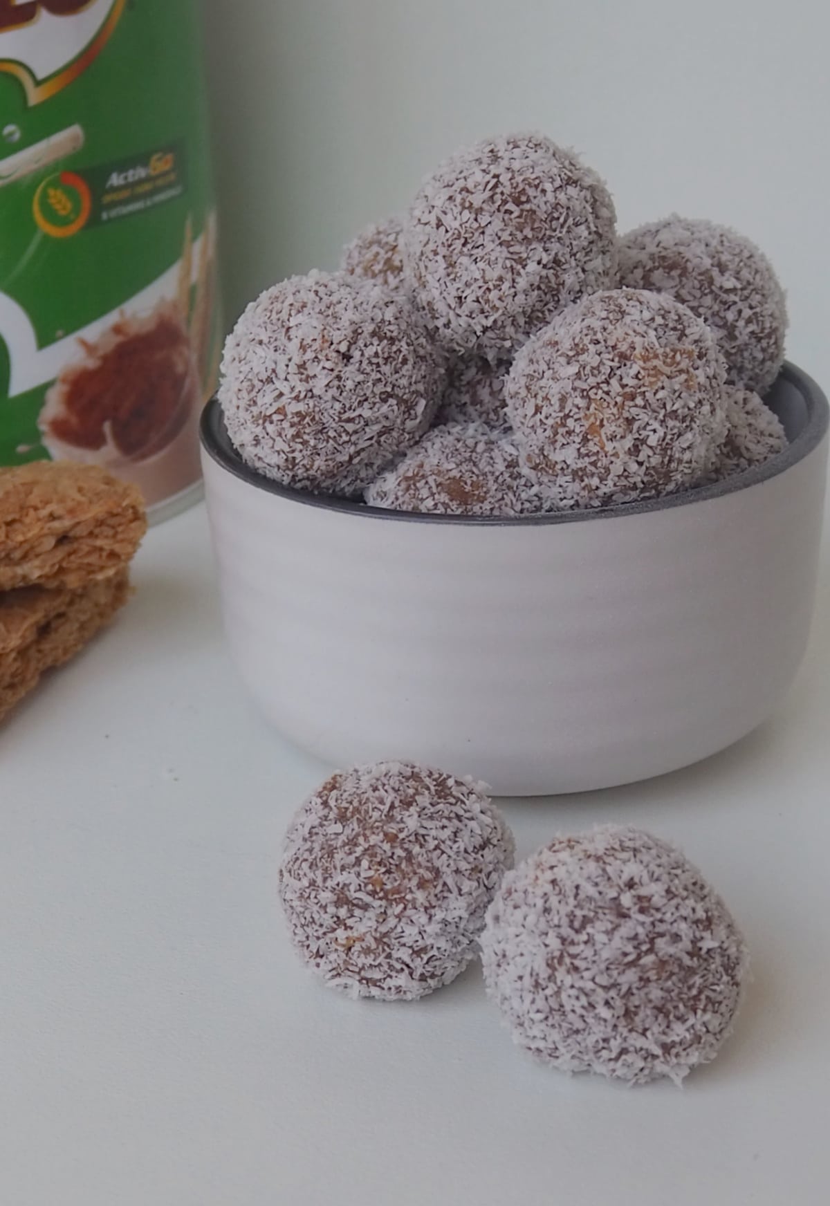 white bowl with grey edging filled with Weet-Bix and Milo Balls. In the background is a jar of Milo and 2 Went-Bix bars.