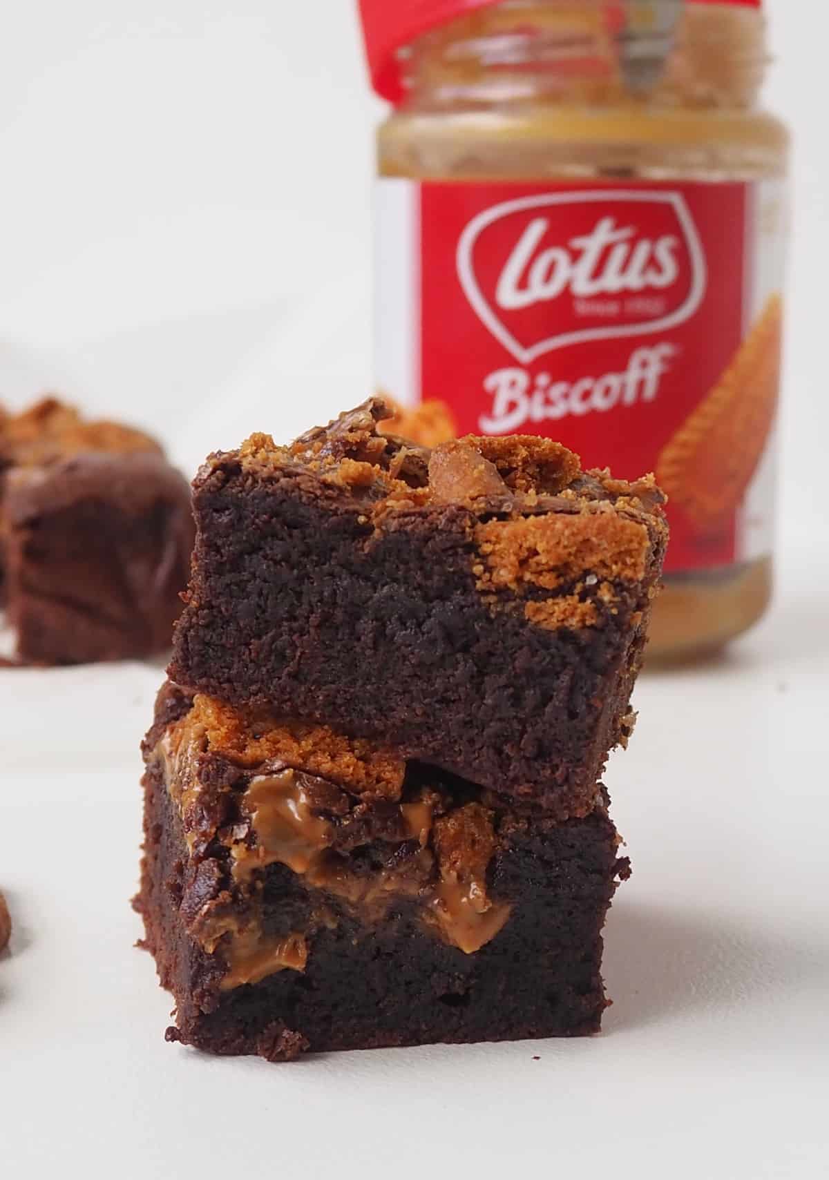 Two slices of biscoff brownies on top of each other. in the background in a jar of biscoff.