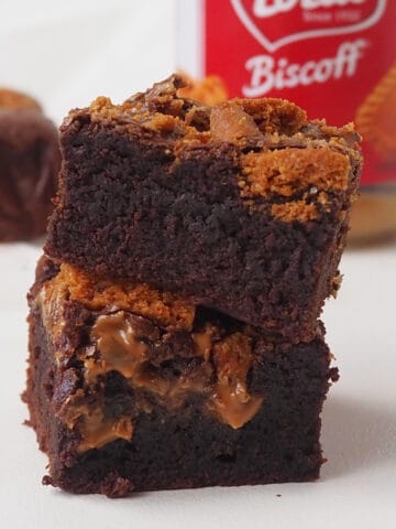 Two slices of biscoff brownies on top of each other. in the background in a jar of biscoff.