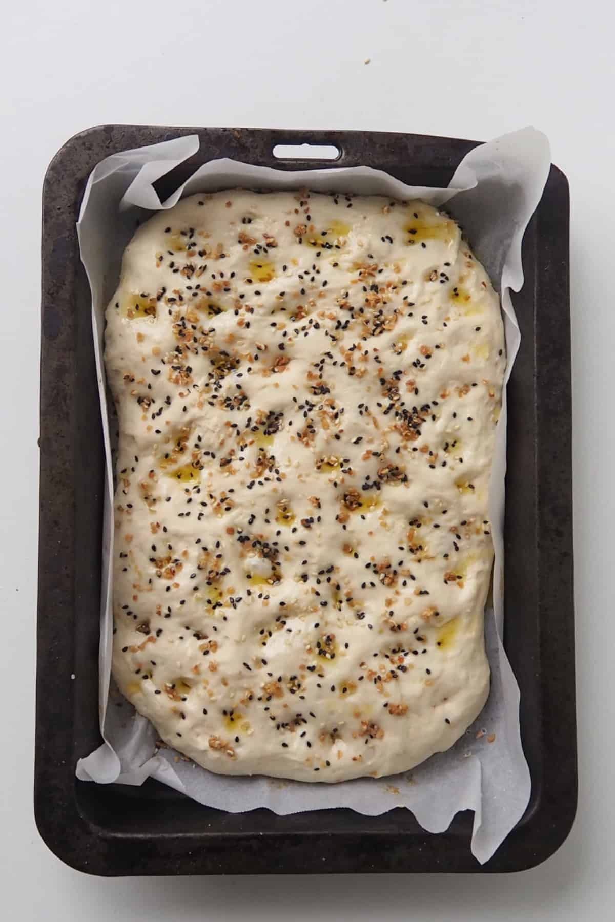 Focaccia dough topped with everything but the bagel seasoning in a baking dish ready to go into the oven.