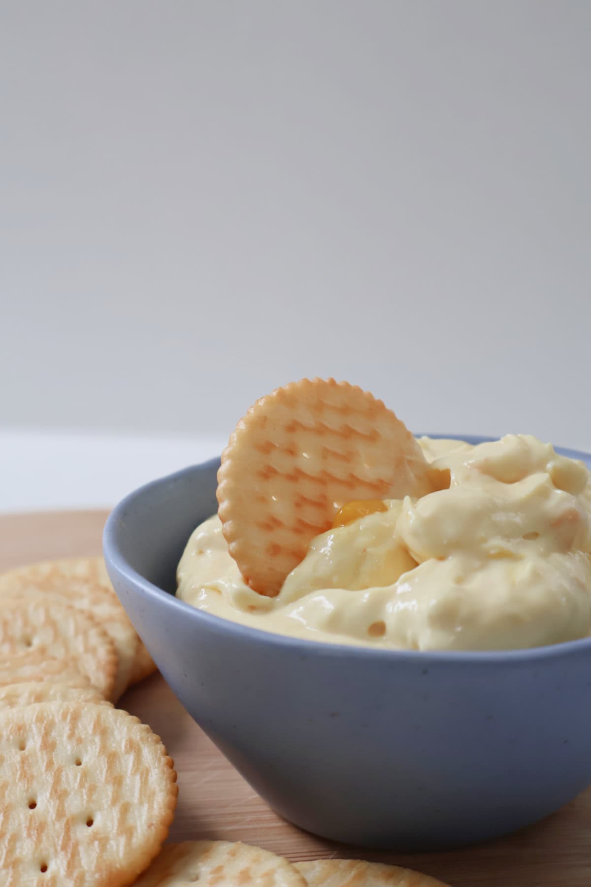 Side view of corn relish dip in a blue bowl. A cracker is sitting in the dip.