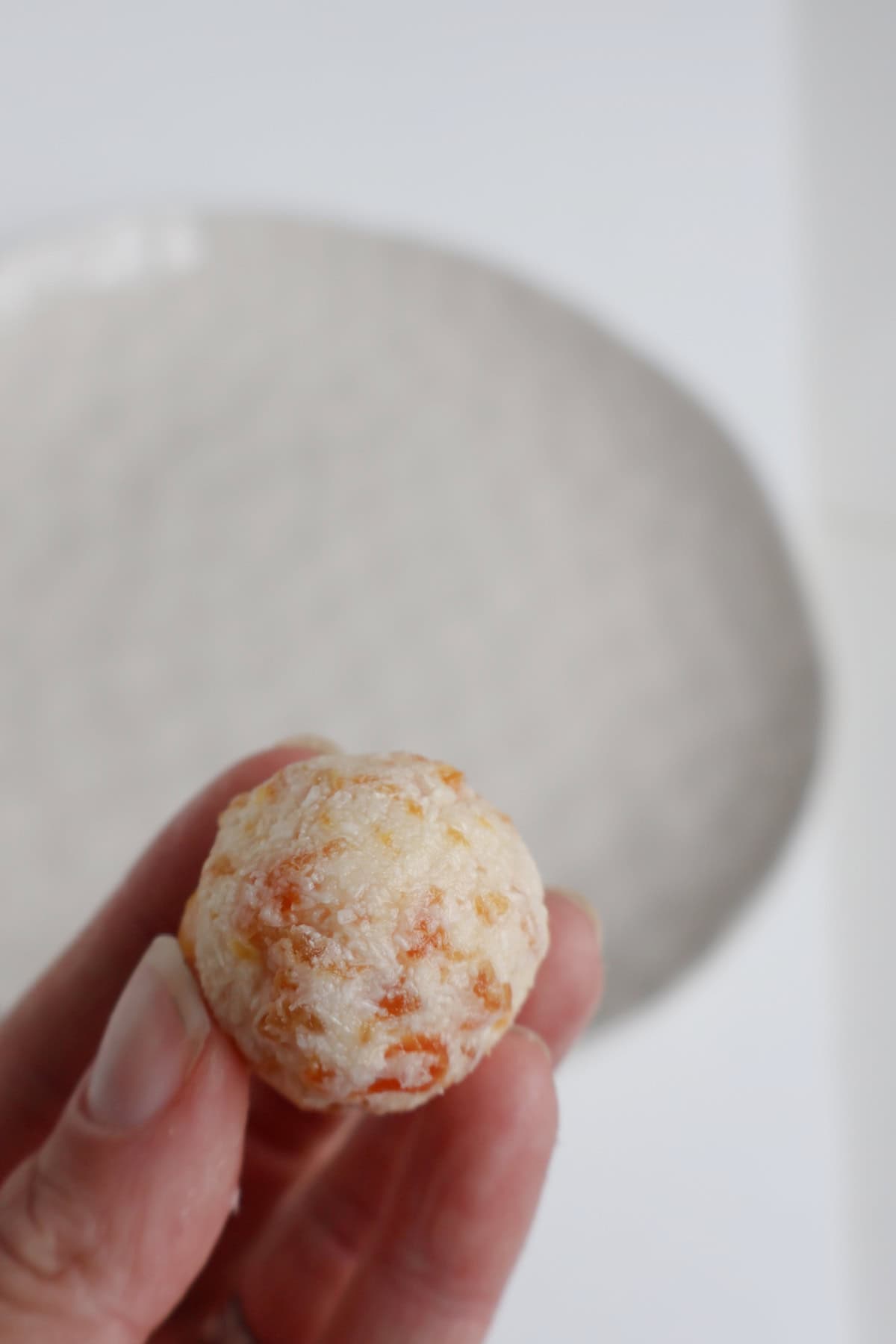 Adult holding a apricot and coconut ball before its rolled in coconut.