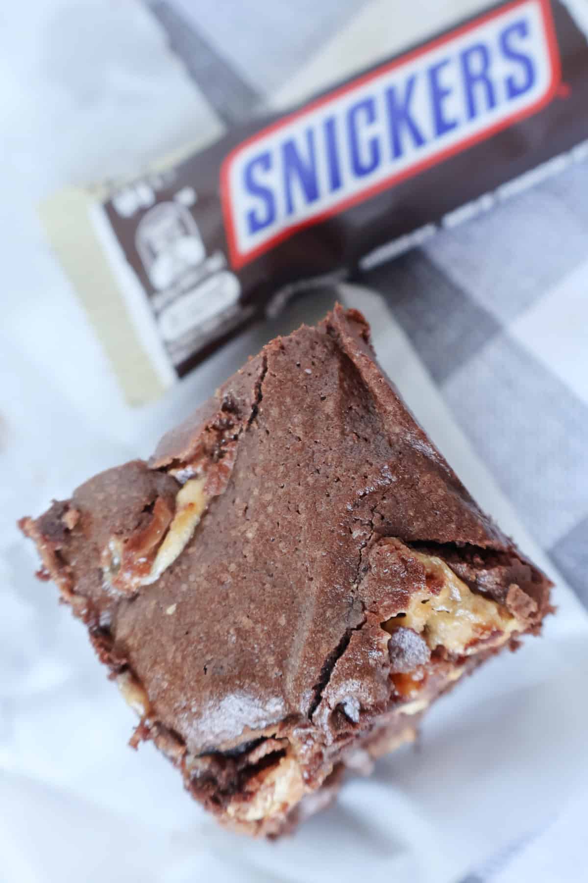 overhead view of piece of Snickers brownie and in back ground is a nickers bar.