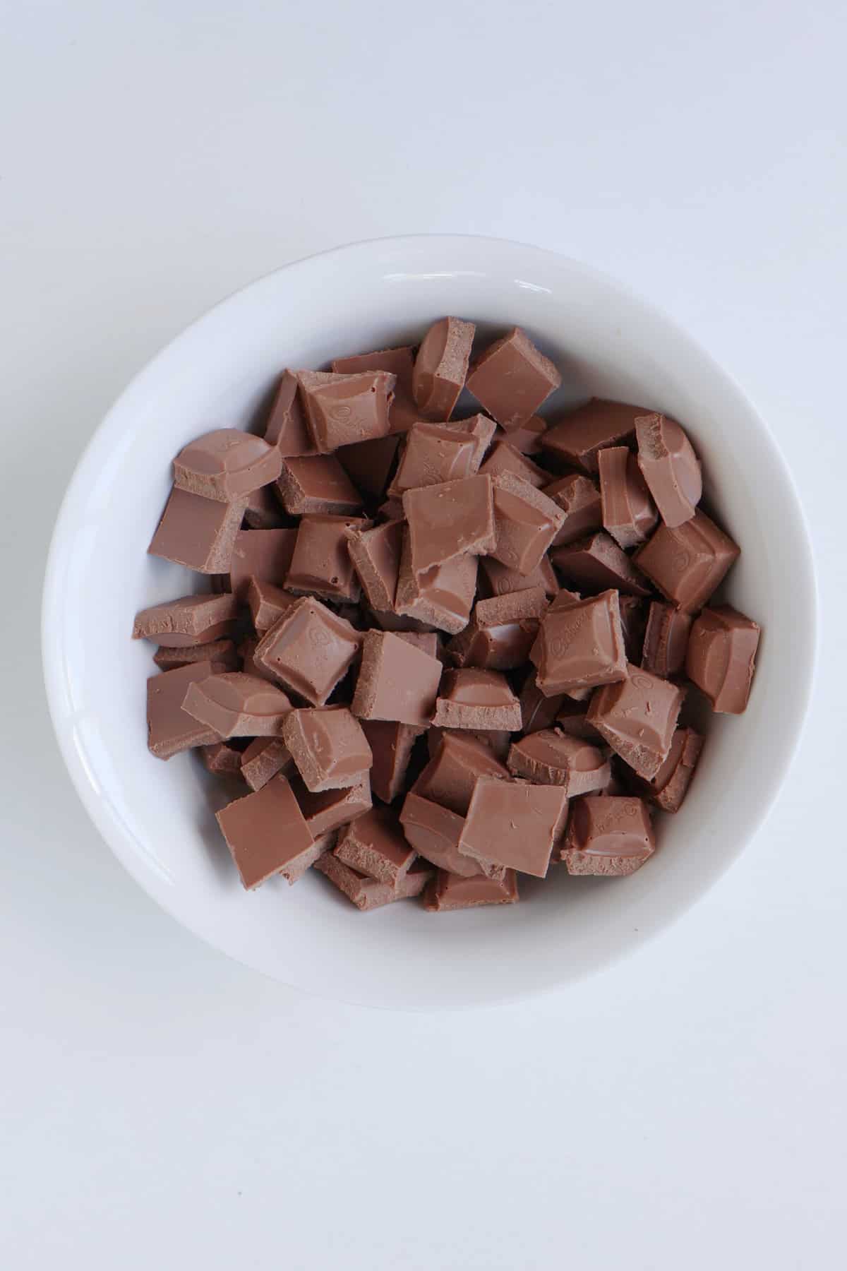 Milk chocolate pieces in a white bowl.