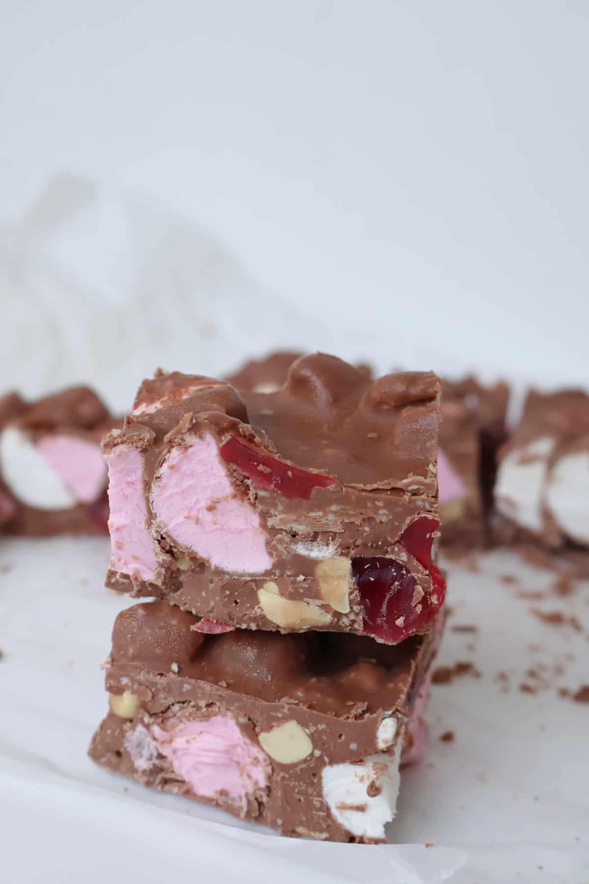 Two pieces of chocolate rocky road on top of each other. In the background is more pieces of rocky road.