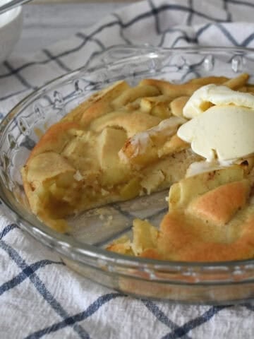 Side view of apple sponge pudding topped with ice cream sitting on a check towel.